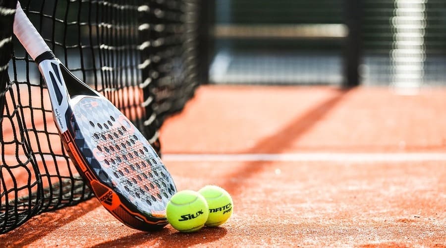 due palline da tennis con una rachetta da padel appoggiata sulla rete