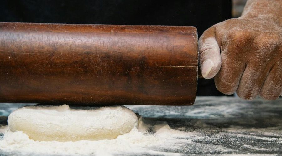 Close-up of a chef rolling dough with a wooden pin, capturing the art of baking.